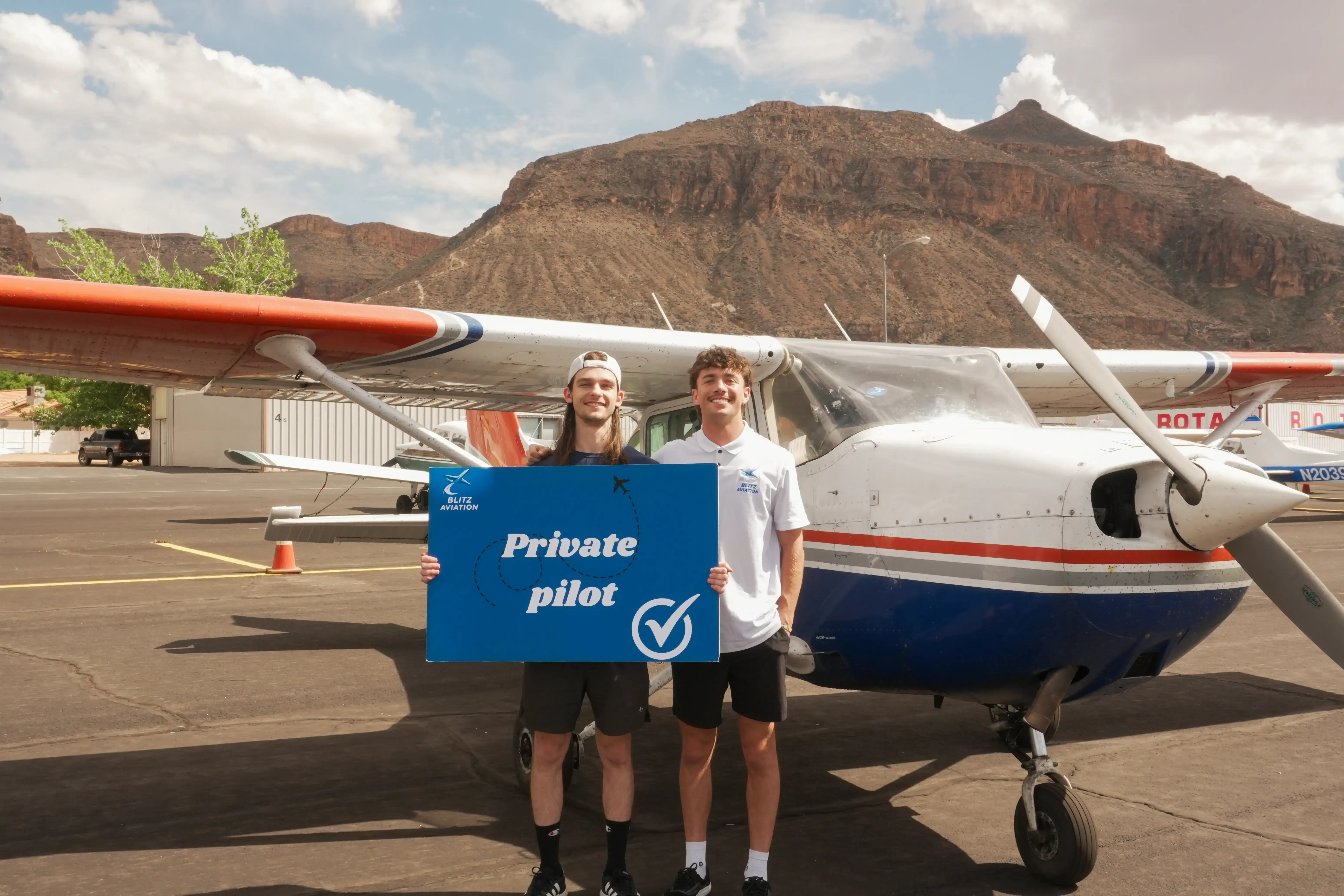 Student and CFI standing in front of an airplane while holding a poster with Passed Private Pilot on it at Blitz Aviation Utah