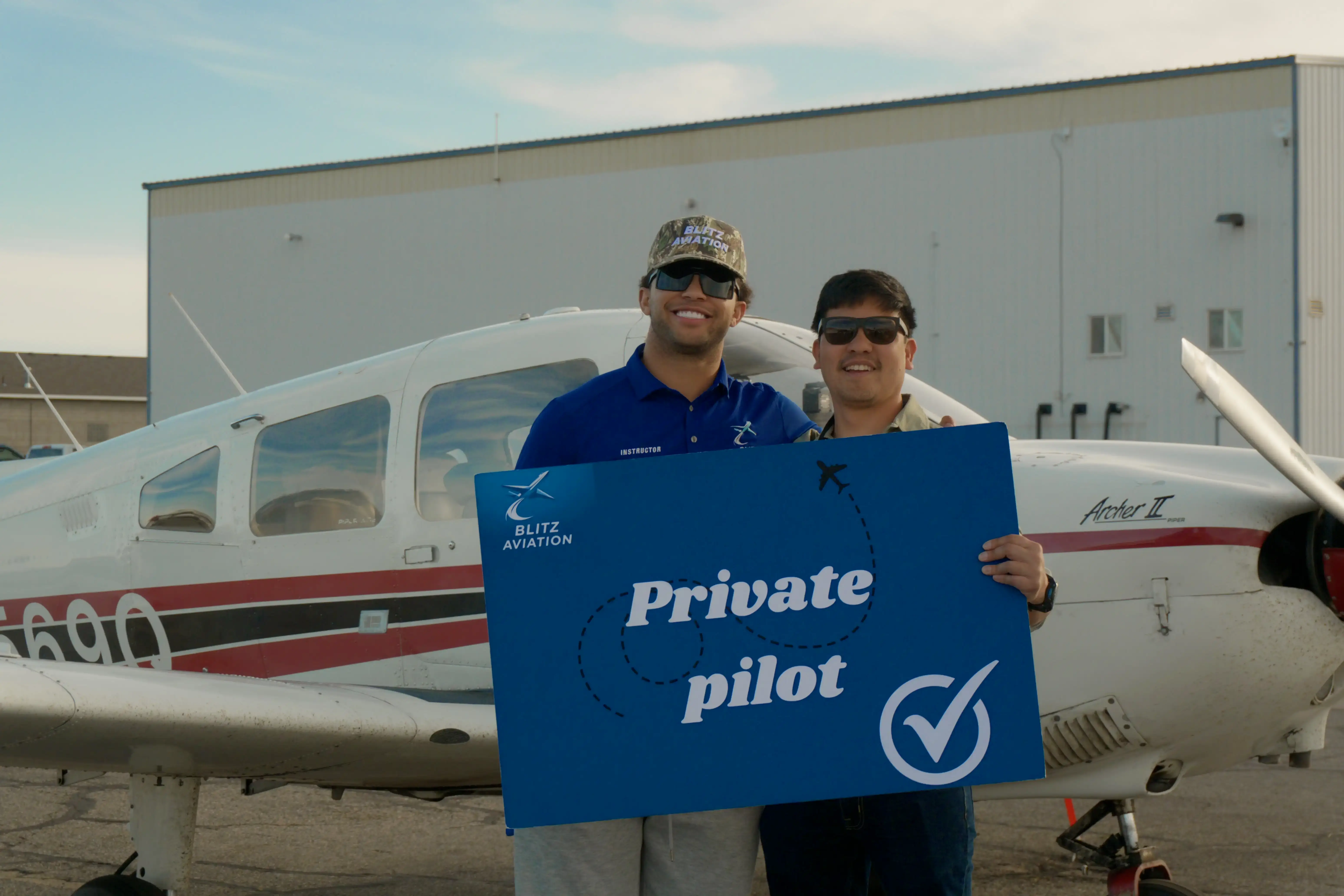 CFI and student in front of an airplane holding a poster with "Private Pilot" written on it