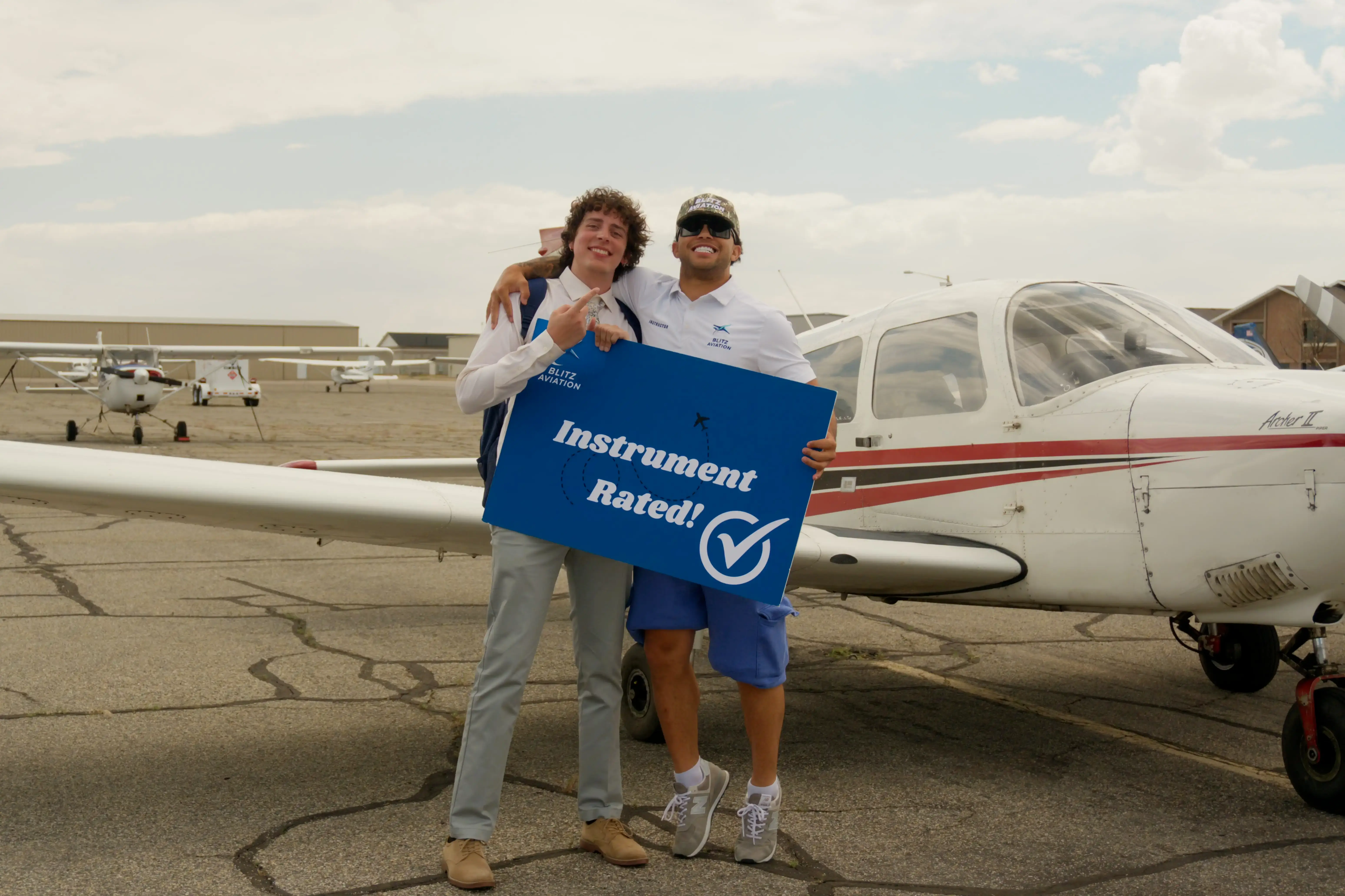 Student and CFI standing in front of an airplane while holding a poster with "Instrument Rated" written on it