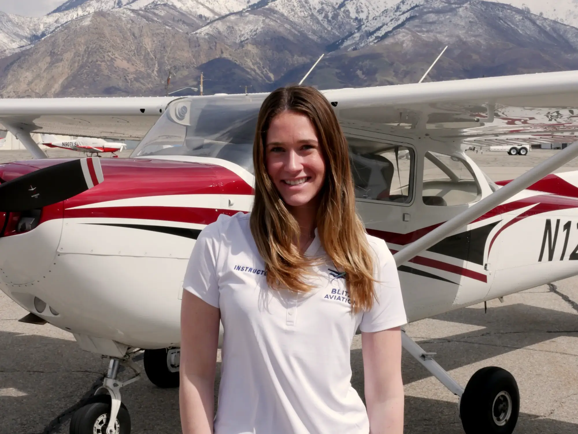 Woman smiling in front of an airplane during daytime with mountains in the background