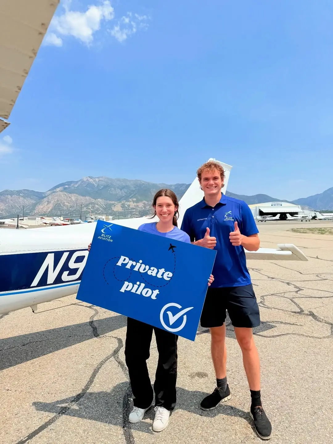 Student and CFI standing in front of an airplane while holding a poster with Passed Private Pilot on it at Blitz Aviation Utah