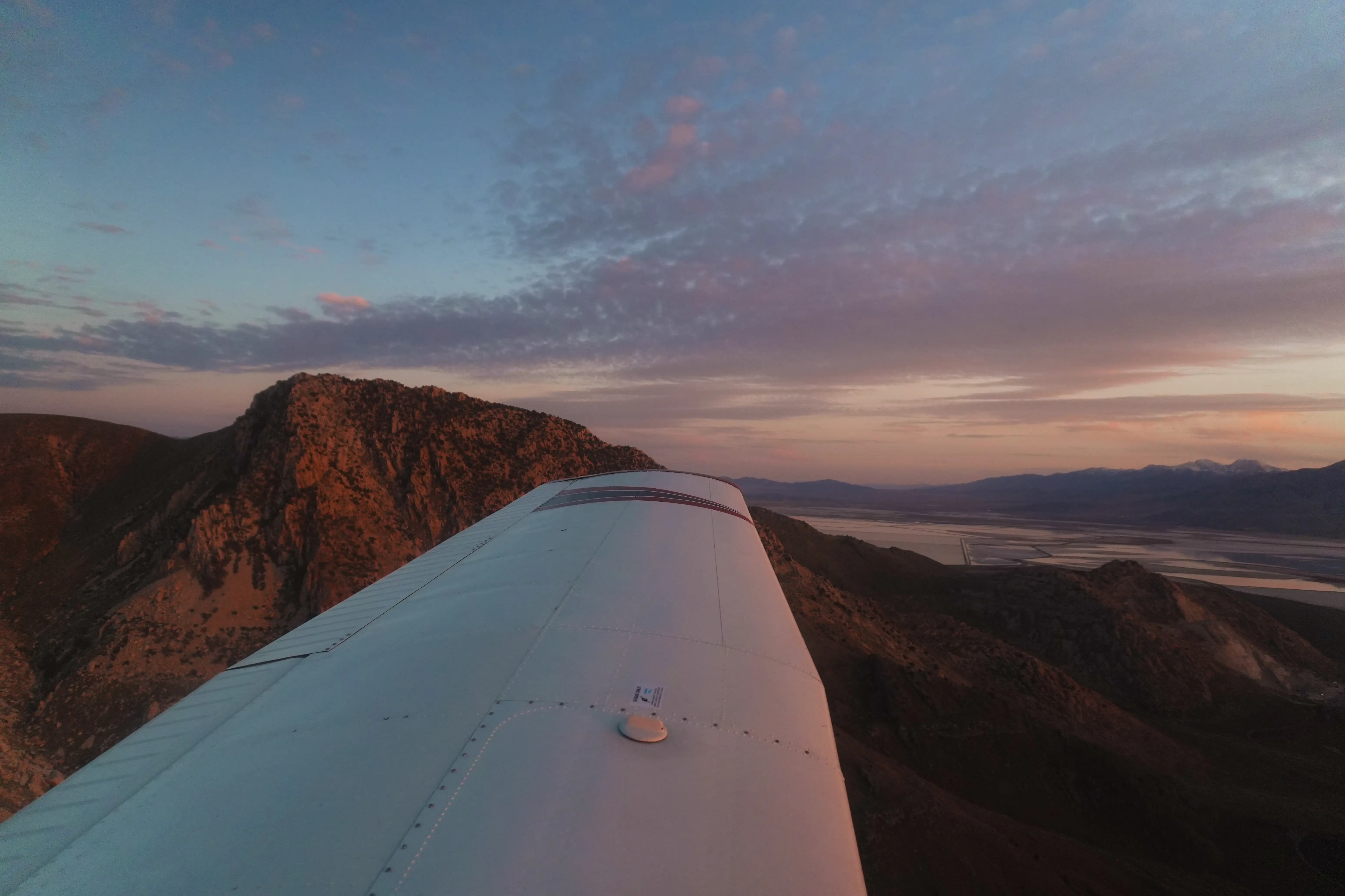 Sunset over the ramp and mountains seen from beside the wing of a Blitz Aviation Cessna